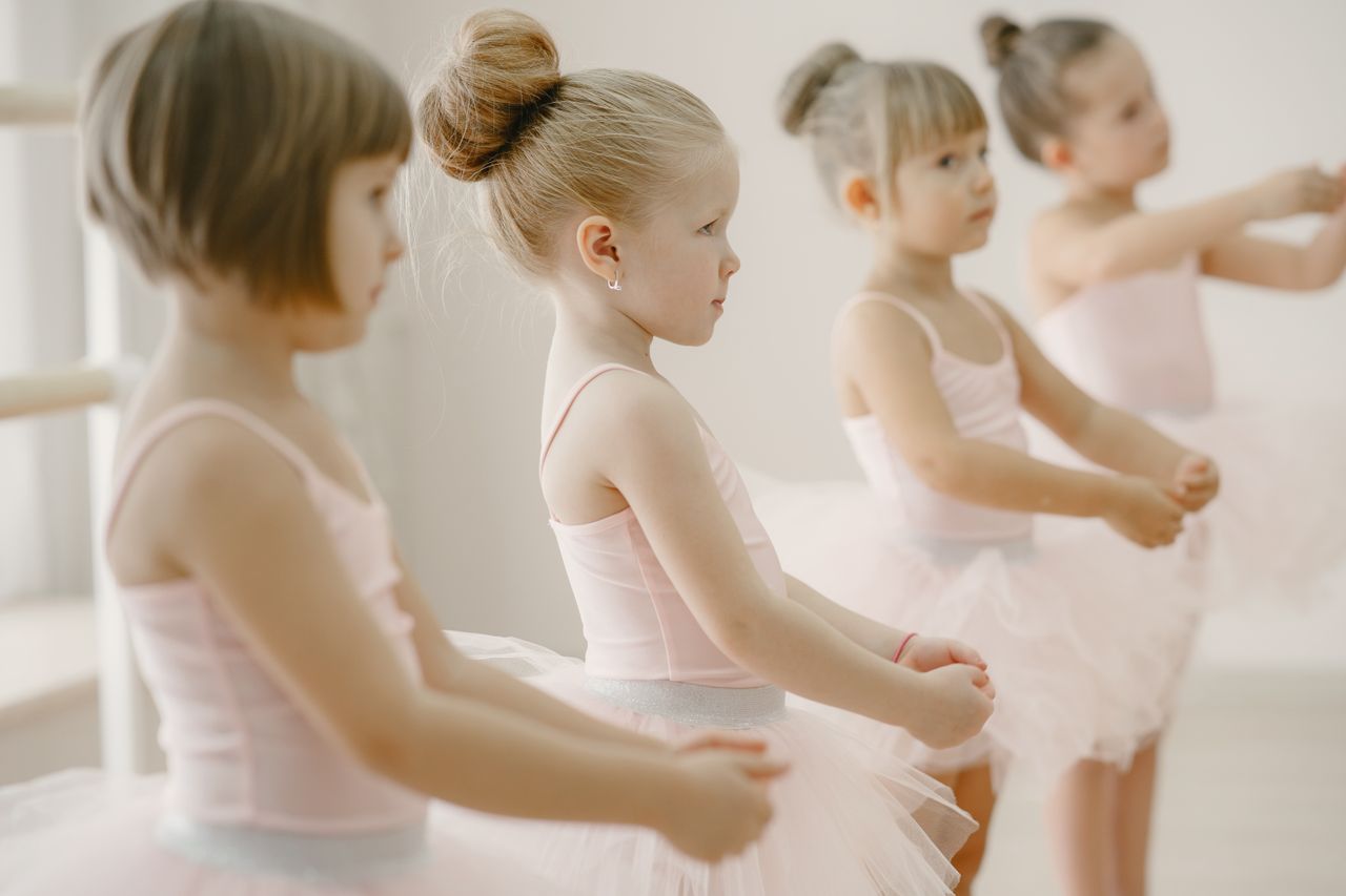 Four young girls in ballet class wearing pink tutus, practicing together.