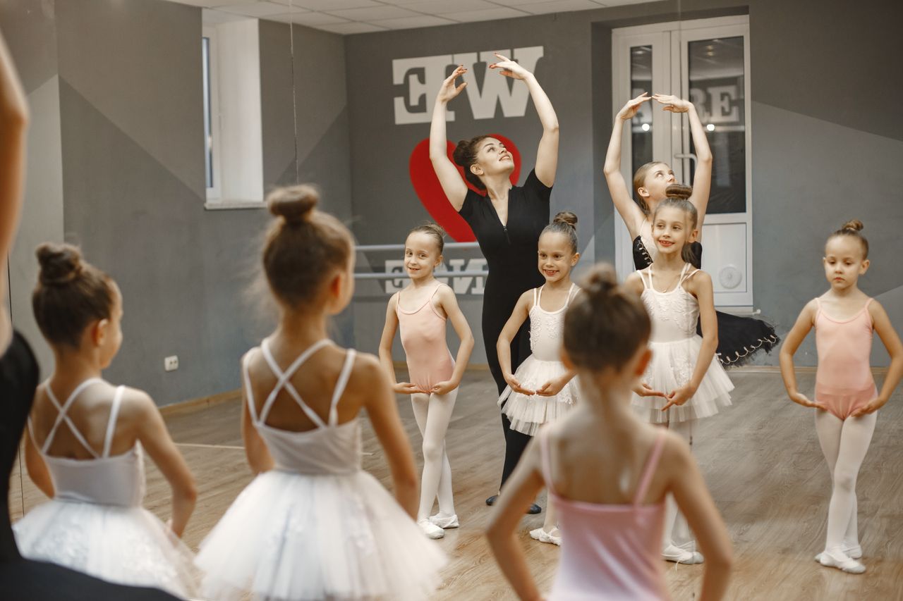 A group of young ballerinas practicing ballet poses under a teachers guidance in a dance studio.